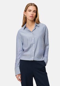 Striped button-up shirt in light blue and white with long sleeves and a relaxed fit, paired with dark pants, showcasing a casual design.