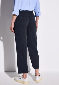 Mörkblå, lätta bomullsbyxor med rak benkjol och två bakfickor. Kombinerat med vita sneakers och en ljusblå skjorta.