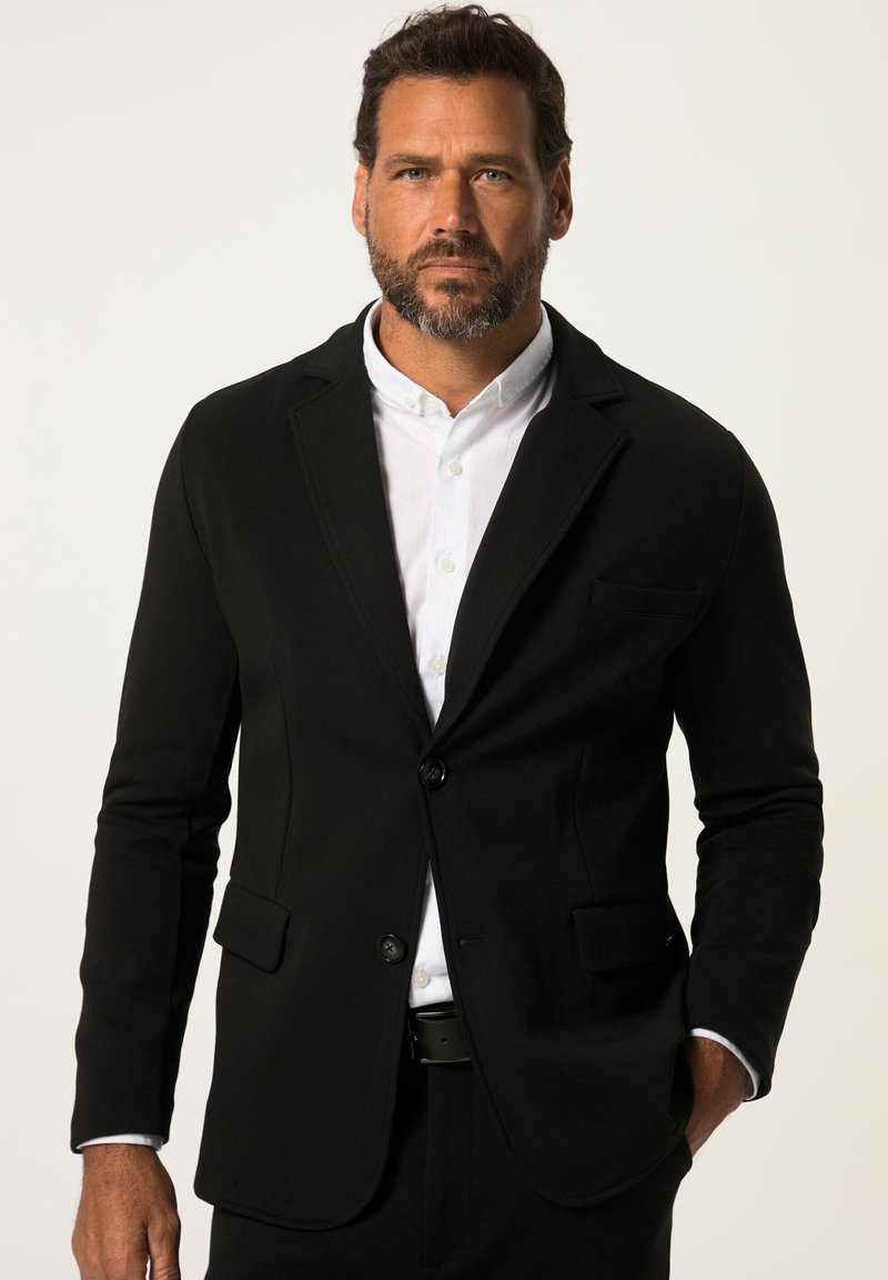 Zwarte op maat gemaakte blazer met twee voorzakken en een enkele knoopsluiting, gedragen over een witte blouse met kraag, met een soepele textuur.