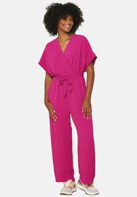 Fuchsia jumpsuit with a wrap design, short sleeves, and a tie belt at the waist. Soft texture and wide, flowing legs.