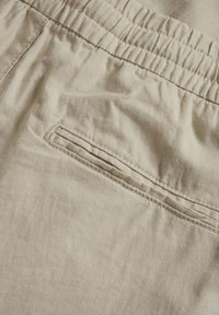 Beiga linbyxor med elastisk midja, en enkel sydd bakficka och en mjuk, texturerad tygfinish.