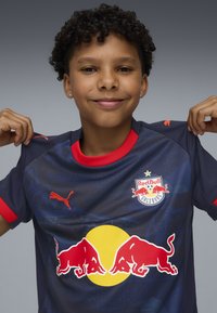 Maillot de sport bleu en matériau synthétique, avec des accents rouges, logo du Red Bull Salzburg, et marquage Puma sur l'épaule.
