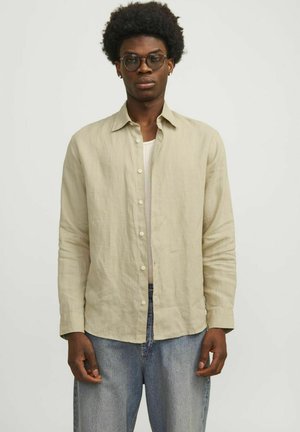 Light beige linen shirt with long sleeves, button front, and collar. Worn over a white undershirt, paired with light blue jeans.