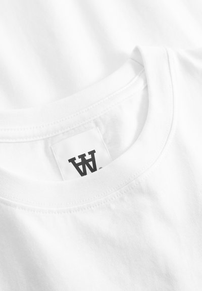 Κοντινό πλάνο για γιακά λευκού βαμβακερού T-shirt με στρογγυλή λαιμόκοψη και μαύρη τυπωμένη ετικέτα της μάρκας στο εσωτερικό.