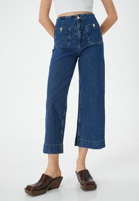 Farkut tummansiniset, korkeavyötäröiset ja laajalahkeiset. Ominaisuuksia ovat kaksinkertaiset etupocketit, kultaiset yksityiskohdat ja siisti viimeistely lahkeessa.