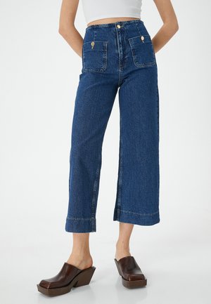 Pantalons en denim taille haute et à jambe large en bleu foncé. Caractéristiques : poches avant doubles, éléments en laiton doré et finition nette au niveau de l'ourlet.