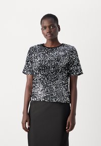 Haut noir à manches courtes recouvert de paillettes argentées brillantes, avec une encolure ronde et une coupe décontractée. Porté avec une jupe noire unie.