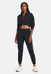 Black athletic outfit featuring a cropped zip-up jacket with a high collar and tapered joggers with side pockets; paired with white sneakers.