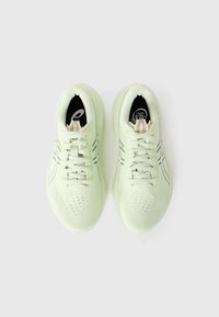 Light green athletic shoes with a textured upper, smooth sole, and reflective accents, featuring laces and perforated detailing for breathability.