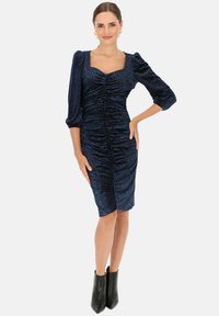 Granatowa sukienka z marszczeniami, ze kwadratowym dekoltem, rękawami o długości 3/4 z bufkami i teksturowanym materiałem, połączona z czarnymi botkami za kostkę.
