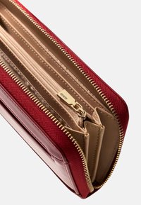 Portafoglio rosso con zip, esterno in tessuto testurizzato, interno liscio color beige, accessori color oro e molteplici scomparti per l'organizzazione.