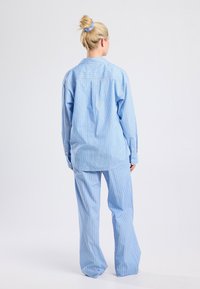 Blue and white striped matching set featuring a loose-fitting shirt and pants. The shirt has a collar and button closure; pants are wide leg.
