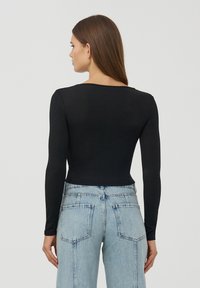 Czarna bluzka z długim rękawem i okrągłym dekoltem, dopasowana, w zestawie z jasnoniebieskimi spodniami o wysokim stanie z prostym krojem i widocznymi kieszeniami.