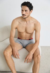 Szürke boxer alsónadrág piros derékrésszel, rajta a "PUMA" logóval; a modell egy textúrált, világos színű szövetfelületen ül.