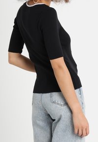 Top negro ajustado con mangas cortas y cuello redondo, con un ribete en contraste. Llevado con jeans de tiro alto en azul claro.