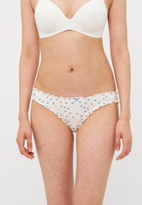 Witte onderbroekjes van stof met blauwe bloemmotieven, golvende randen en een lichtblauw lintdetail aan de voorkant. Zachte textuur, laag uitgesneden ontwerp.