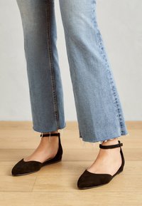 Svarta mocka balletlägenheter med spetsig tå och ankelrem, kombinerat med ljusa denim jeans med utsvängd nederdel och fransad fåll.