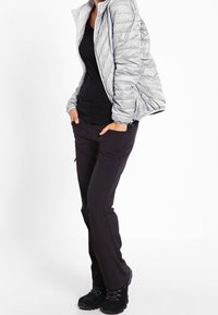 Szara puchowa kurtka z pikowanym wzorem, czarny top, czarne spodnie z kieszeniami oraz czarne buty do wędrówek. Teksturowane materiały podkreślają wizualny kontrast.