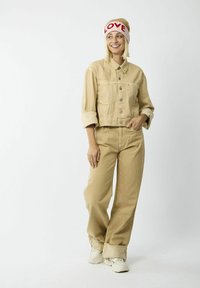 Beige denim jack met knoopsluiting en opgerolde mouwen, gecombineerd met bijpassende hoge taille beige jeans. Geaccessoireerd met een gebreide muts met "LOVE" in het rood.