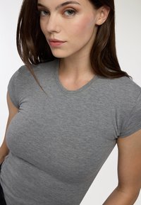 T-shirt grigio aderente con maniche corte e colletto a girocollo. Il tessuto ha una consistenza morbida e una leggera elasticità, che consente un indossamento confortevole.