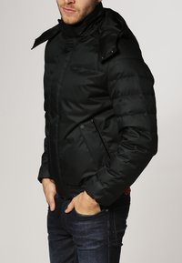 Chaqueta acolchada negra con cuello alto, textura acolchada y cremallera frontal. Cuenta con bolsillos laterales y cintura elástica.