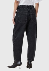 Pantaloni in denim neri a vita alta con una cintura elastica, vestibilità rilassata e due tasche posteriori, abbinati a stivali neri alla caviglia.