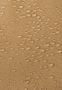Tessuto beige con una superficie texture, caratterizzato da numerose gocce d'acqua trasparenti di varie dimensioni sparse su tutto il materiale.