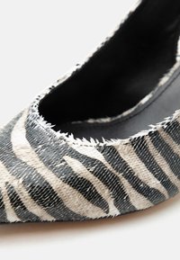 Πέδιλο υψηλού τακουνιού σε μοτίβο ζέβρας ασπρόμαυρο, με υφή που μοιάζει με λέπια και μυτερή μύτη.