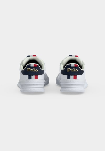 Para białych sneakersów Polo Ralph Lauren, pokazująca widok tylnej części, z granatową łatką na pięcie, czerwoną i białą paskowaną pętelką i złotym napisem "Polo".