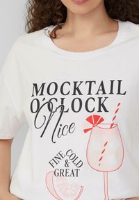 Witte katoenen t-shirt met een drankgrafiek en rode en zwarte tekst die "MOCKTAIL O'CLOCK Nice" en "FINE COLD & GREAT" leest. Ronde halslijn.