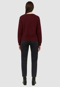 Maglione a maglia bordeaux con una silhouette morbida, caratterizzato da un collo rotondo e maniche lunghe, abbinato a jeans scuri e stivaletti.