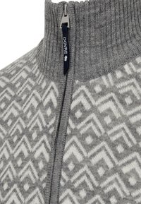 Grå zip-up sweater med en tykk ribstrikket krave. Har geometriske hvide mønstre og et stofmærke nær lynlåsen med teksten "DOVRE."