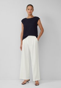 Haut en tricot texturé bleu marine à manches courtes, associé à un pantalon large blanc et décontracté, et des talons noirs à lanières. Design simple et contemporain.