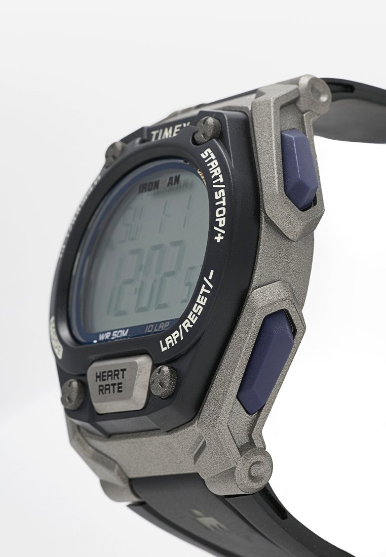 Reloj deportivo digital con un diseño de plástico negro y plata, que cuenta con una gran pantalla, botones morados y una correa negra texturizada.