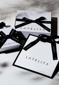 Drei Geschenkboxen mit glanzweisser Oberfläche, schwarzem Band und "LATELITA"-Logo. Die grösste Box verfügt über einen schwarzen Rand.