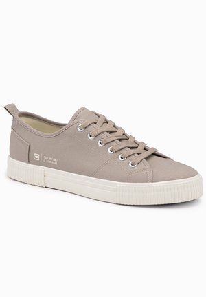 Beige canvas sneakers med rund tås, vit gummisul och kontrasterande texturerad rand. Har ögla och bakre dragtag.