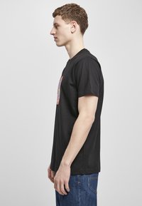 Svart bomull T-skjorte med korte ermer, med et fargerikt grafisk motiv på framsiden. Brukt sammen med blå denimjeans.