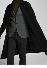 Svart ullblandad kappa, öppen för att avslöja en grå houndstooth-väst under. Outfitten kombineras med svarta byxor som har en slank design.