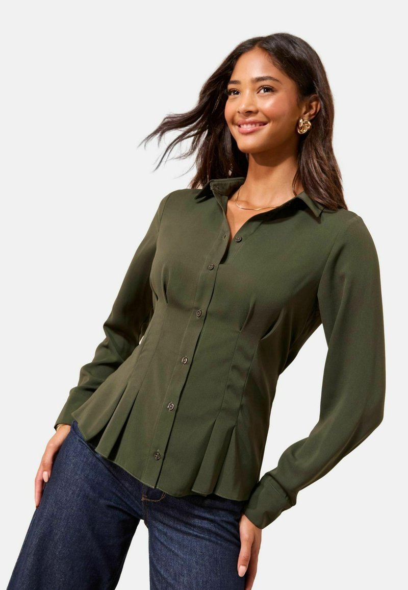 Cămașă verde cu nasturi, design plisat, mâneci lungi și guler. Țesătura pare netedă, completând o pereche de blugi din denim închis la culoare.