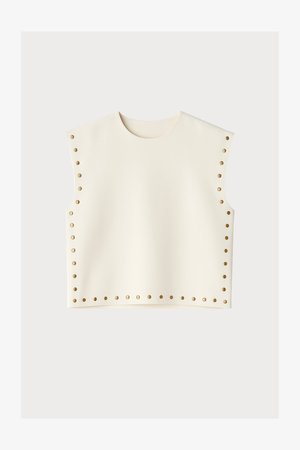 Top senza maniche color crema con scollo rotondo e piccoli borchie dorate distribuite uniformemente lungo i lati e l'orlo inferiore.