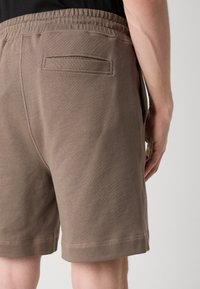 Shorts en coton marron avec une finition texturée, taille élastique et poche latérale. L'ourlet se termine par un léger détail de couture.