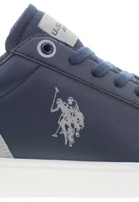 Marinblå syntetiska sneakers med ljusgrå detaljer, utrustade med en strukturerad vit sula och en metallisk logotyp med två polo-spelare på hästar.