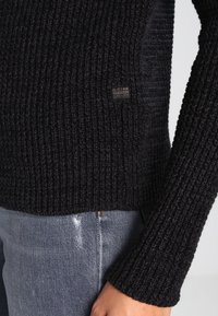 Jersey negro de punto con textura acanalada, que presenta una pequeña etiqueta de G-Star en el lateral. Las mangas largas y el diseño ajustado complementan perfectamente los vaqueros.