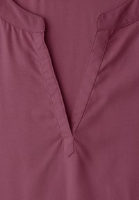 Gros plan sur un shirt mauve à col en V avec un col étroit et des surpiqûres visibles le long de l'encolure.