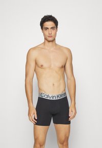 Black boxer briefs with a grey Calvin Klein waistband. Made from a soft material, featuring a fitted design and minimal seams for comfort.