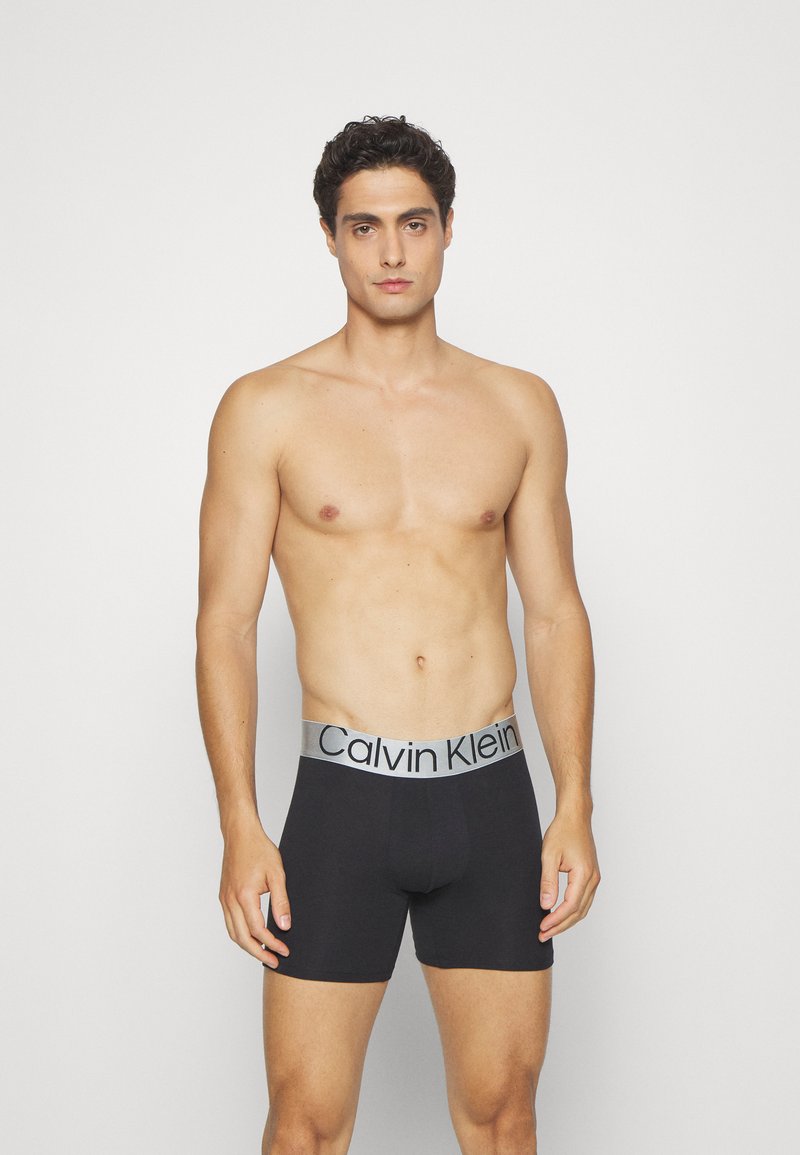 Black boxer briefs with a grey Calvin Klein waistband. Made from a soft material, featuring a fitted design and minimal seams for comfort.