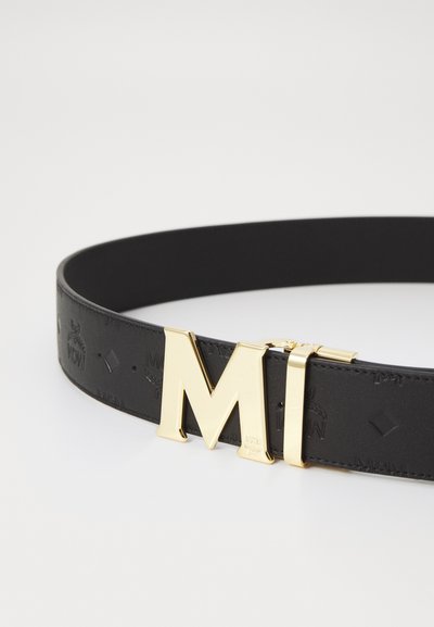 Schwarzer Ledergürtel mit geprägtem Logo-Muster, ausgestattet mit einer großen goldenen Metall-Schnalle in Form eines "M" zur Befestigung. Glatte Textur mit einem eleganten Design.