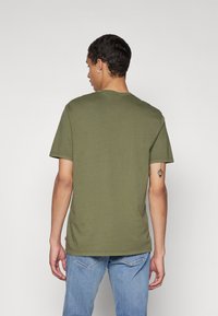 Oliwkowa bawełniana koszulka z krótkim rękawem i okrągłym dekoltem. Posiada gładką teksturę i dół, który opada poniżej talii.