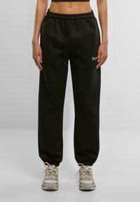 Pantalons de survêtement noirs avec une taille élastique et un cordon de serrage. Hems resserrés. Petit logo blanc sur la cuisse gauche. Convient pour un usage décontracté.