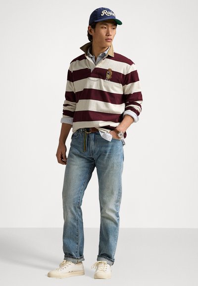 Langermet stripet polo i burgunder og hvit, jeans i denim, hvite sneakers, og en marineblå caps med hvit tekst. Merkelig krage og belte.
